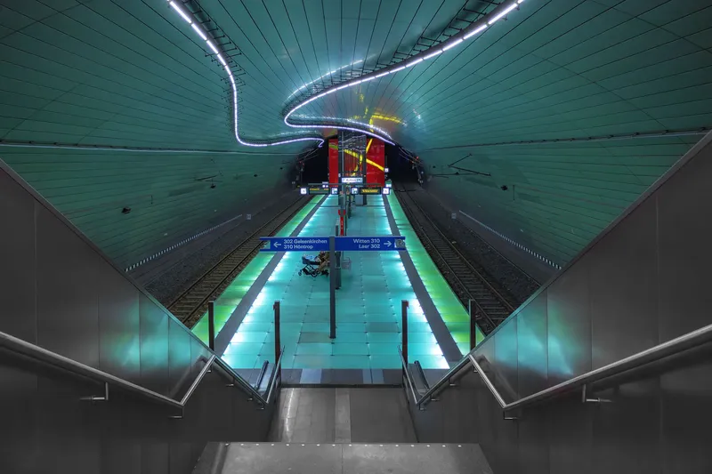 Moderne U-Bahn-Station mit futuristischer Architektur in Deutschland. Beeindruckende türkisfarbene LED-Beleuchtung, grün illuminierter Bahnsteig und geschwungene Deckenführung charakterisieren diese architektonisch einzigartige Station der Linien 302 und 310. Ein Beispiel zeitgenössischer Verkehrsarchitektur.
