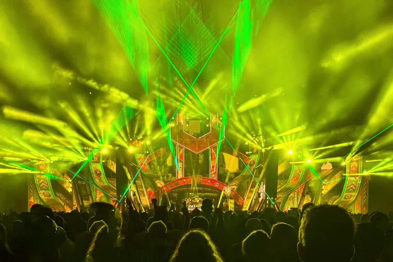 Musikfestival mit gelben Lichtern und grünen Lasern bei Nacht
