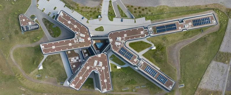 Spektakuläre Luftaufnahme des Amprion-Hauptsitzes: Innovative X-förmige Architektur vereint mit nachhaltiger Bauweise durch Solartechnologie. Der moderne Gebäudekomplex präsentiert sich eingebettet in eine grüne Umgebung mit durchdachter Infrastruktur.
